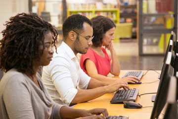 Row of concentrated students using computers at library. Thoughtful young people searching information with help of computers. Education, technology concept