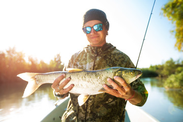 Happy angler holds Asp fish (Aspius aspius) being on the boat and smiles. Astrakhan region, Russia