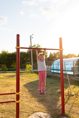 A small child goes in for sports in the stadium. hanging on the horizontal bar, on the uneven bars