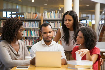 Concentrated young people reading information from laptop. Cheerful students working with laptop at...