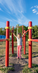 Fototapeta premium A small child goes in for sports in the stadium. hanging on the horizontal bar, on the uneven bars
