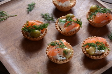 Tartalets with fresh salmon, philadelphia cream cheese, olives on wooden background