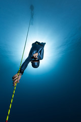 Freediver descends along the rope into the depth while another freediver relaxes on the buoy