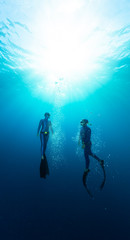 Two freedivers ascend from the depth surrounded by bubbles
