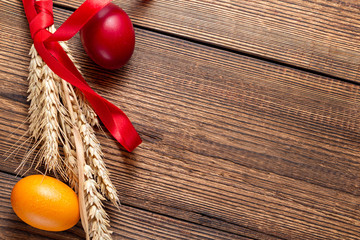 colorful eggs for Easter with ears of grain on brown wooden background