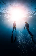 Fotobehang Two freedivers ascend from the depth surrounded by bubbles © Dudarev Mikhail