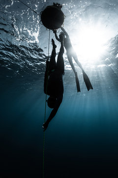 Freediver descends along the rope into the depth while another freediver relaxes on the buoy