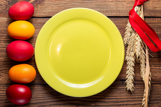 colorful eggs for Easter yellow plate with ears of grain, on brown wooden background