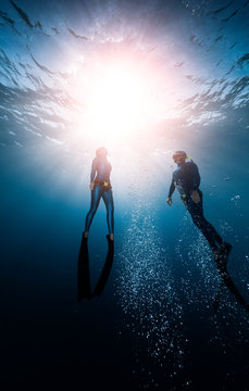 Two freedivers ascend from the depth surrounded by bubbles
