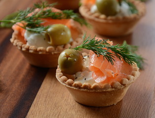 Tartalets with fresh salmon, philadelphia cream cheese, olives on wooden background