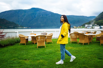 Young woman enjoys picturesque landscape. The girl tourist in a yellow jacket posing against the backdrop of the mountains and lake in the Norway. Travelling, lifestyle, adventure, concept.