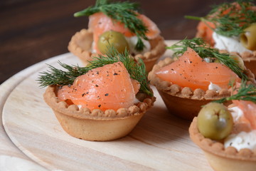 Tartalets with fresh salmon, philadelphia cream cheese, olives on wooden background