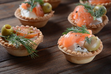 Tartalets with fresh salmon, philadelphia cream cheese, olives on wooden background