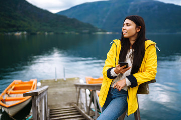 The girl tourist takes a photo on the phone by the lake in Norway. Young woman takes selfie against...