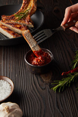 Cropped view of woman putting steak slice in tomato sauce by garlic and salt on wooden surface