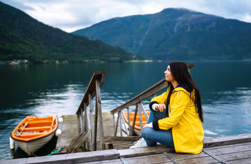 The girl tourist in a yellow jacket posing by the lake in Norway. Active woman relaxing and enjoys freedom near the boat by the lake against the backdrop of the mountains. Travelling, lifestyle.