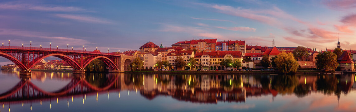 Amazing view of Maribor Old city, Main bridge (Stari most) on the Drava river before sunrise, Slovenia. Scenic cityscape with color sky and reflection, travel background for wallpaper, large panorama © larauhryn