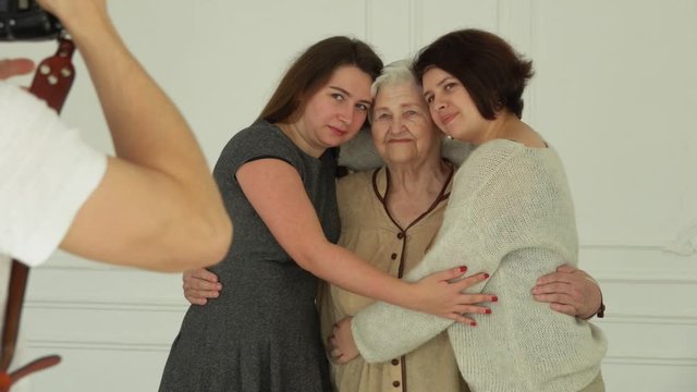 Photographer is taking pictures of an elderly white-haired woman hugging her granddaughters. The beautiful multi-generations family enjoys togetherness 