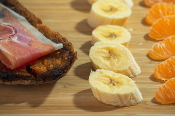 Mediterranean Breakfast. A plate filled with bread and ham, and fruit like tangerine and banana.