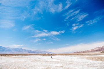 A beautiful woman with hat and summer dress in white and yellow blue walks runs jumps and enjoys the desert landscape of Death Valley in California USA