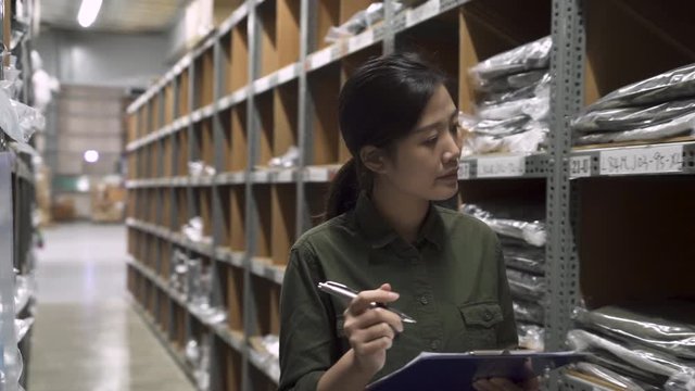 Candid of young attractive asian korean woman auditor staff work walking looking up stock taking inventory in warehouse by writing on clipboard making notes. female owner and small business concept.