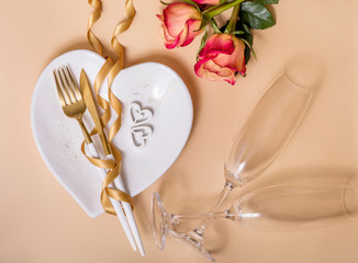 Romantic dinner table setting with roses, champagne glasses, heart shaped plate and golden ribbon,...