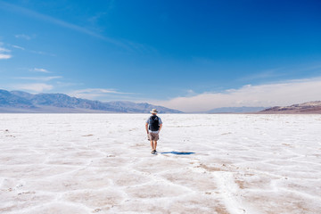 A tourist man with a hat to curb from the sun and a traveler's backpack enjoys a sunny day in the Death Valley desert