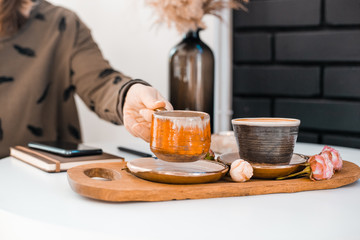 Girl's hand takes a cup of coffee from a wooden tray decorated with rosebuds located on a white table