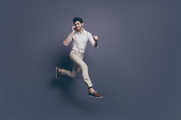 Fototapeta na wymiar Full body profile side photo of excited guy speak smart phone listen discounts win lottery jump run wear white shirt pants trousers isolated over grey color background
