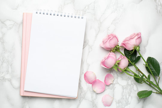 Beautiful pink roses flower and notebook on marble background.Minimalistic composition for the holidays,valentines day and womens day.
