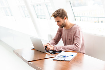Fototapeta premium Image of young man wearing earbuds working on laptop in cafe indoors