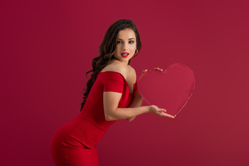 seductive, elegant girl holding paper heart and looking at camera isolated on red