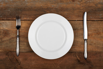 Empty plate with fork and knife on the vintage wooden table