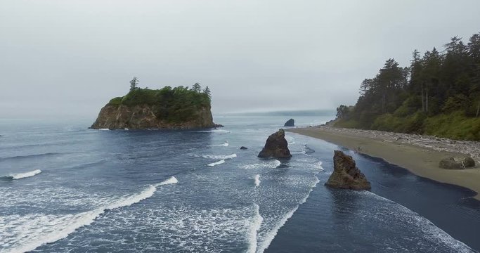Drone camera approaches cliffs protruding from waves on the ocean (Ruby Beach, Olympic National Park, Washington, USA)