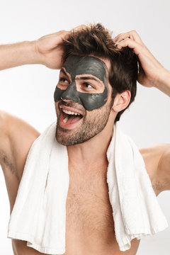 Photo of happy half-naked man with cosmetic mask and towel laughing