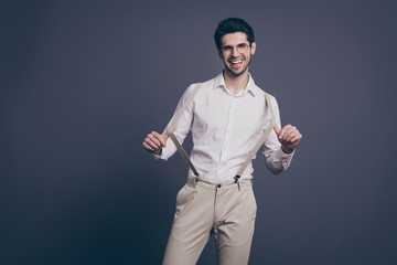 Portrait of his he nice attractive professional imposing cheerful cheery positive brunet guy pulling suspenders having fun isolated on grey pastel color background