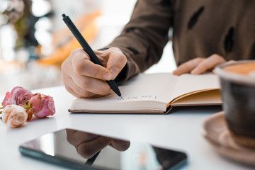 Girl writes I love you in a notebook on a table next to a phone and a cup of coffee decorated with...