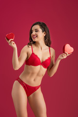 sexy, smiling girl in lingerie holding heart-shaped gift boxes isolated on red