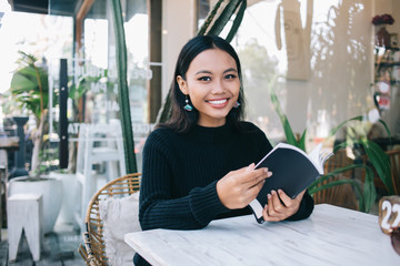 Cheerful Indonesian woman at table with menu in cafe