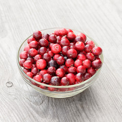 The fresh dirty cranberry in the glass bowl on the wooden texture.