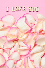 The inscription I love you in the center of a background of rose petals in white and pink. Paper background. Vertical.