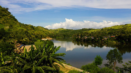 Fototapeta na wymiar River and green hills. Beautiful natural scenery of river in southeast Asia. Countryside on a large tropical island. Small village on the green hills by the river. The nature of the Philippines, Samar