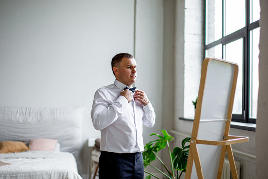 the groom dresses in front of the mirror