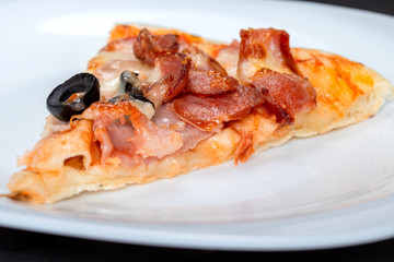 slice of pizza with bacon cheese and olives lies on a plate