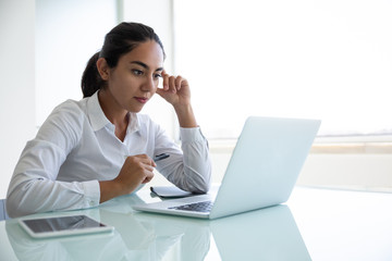 Concentrated young businesswoman using laptop in office. Focused young businesswoman sitting at...