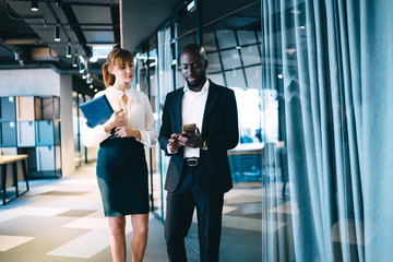 Pensive diverse coworkers interacting with smartphone in corridor of cozy modern office