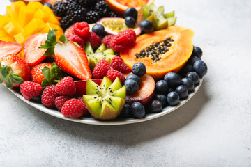 Delicious fruit platter pomegranate papaya oranges grapes berries on plate on white, selective focus