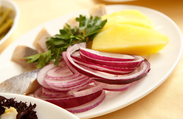 Onion, sliced in half rings, boiled potatoes and herring on a plate
