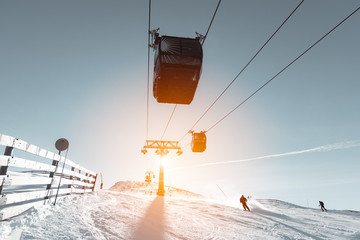 Ski slope with skier and cable car pylon in sun backlight