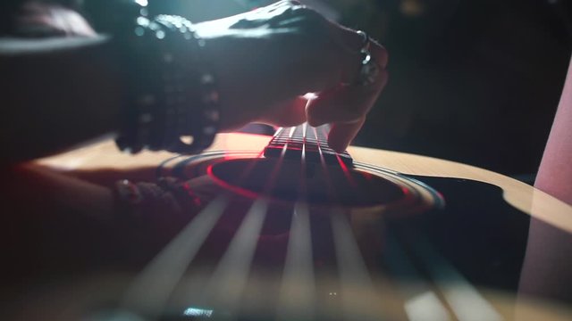 The musician hand goes over the strings while playing the guitar. 